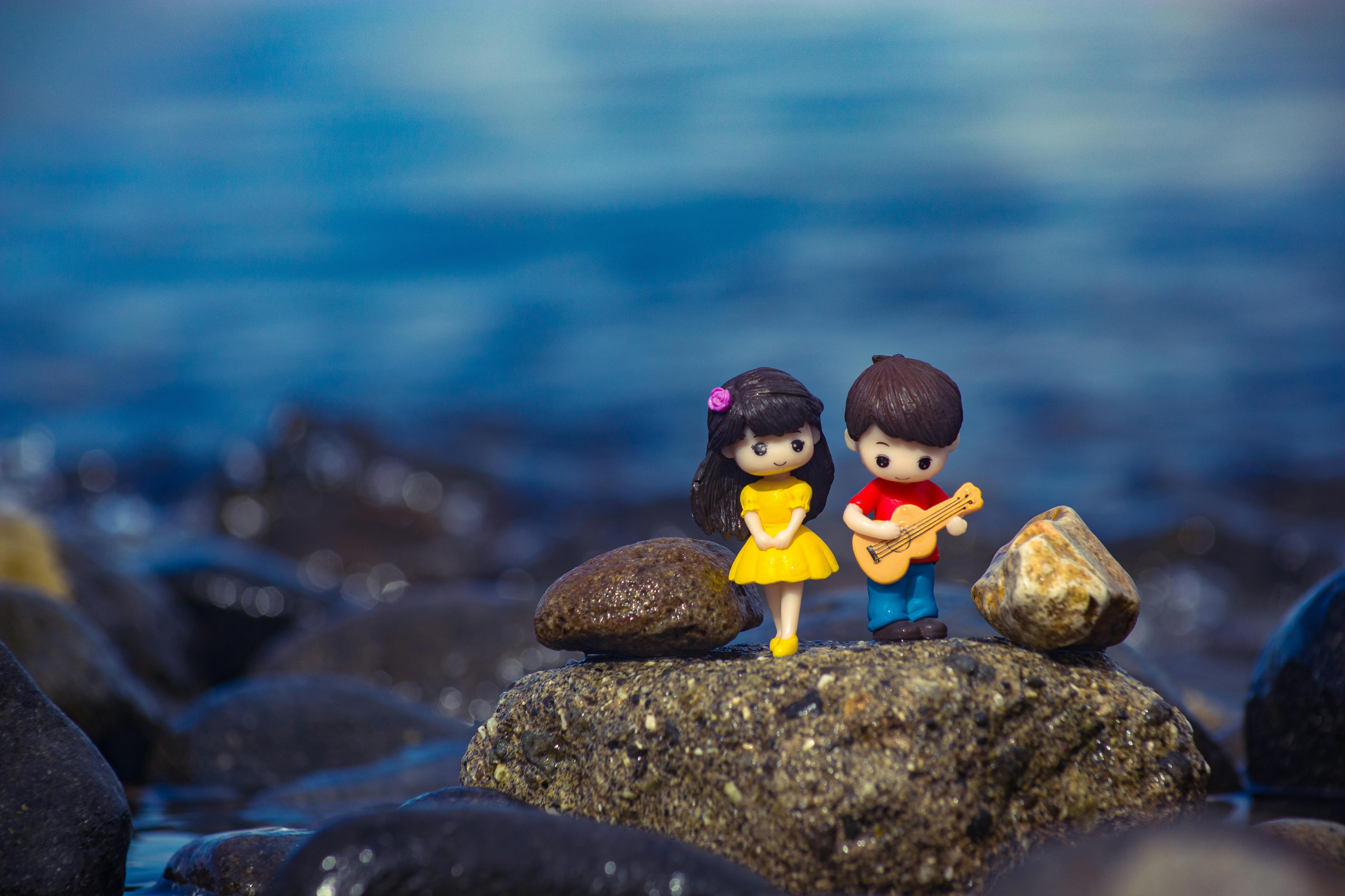 pexels-photo-10010700-10010700 Adorable clay figures of a couple with a guitar on a rocky shore, set against a serene body of water.
